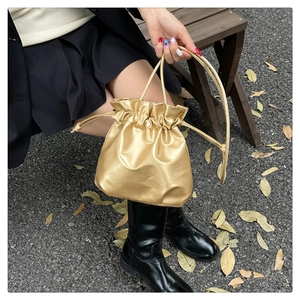 Detail of metallic gold drawstring bucket bag in soft faux leather with pleated finish