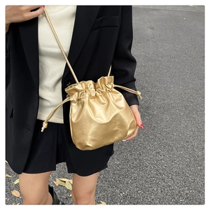 Close-up of golden drawstring bucket bag with metallic texture on a black blazer outfit