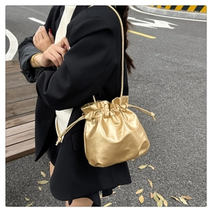 Close-up of stylish metallic gold drawstring bucket bag worn over a black blazer