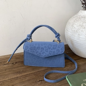 Blue suede crossbody bag with subtle leopard pattern and knotted handle design
