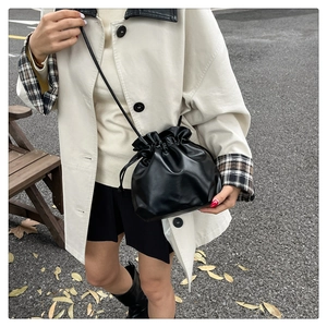 Detail of black drawstring bucket bag in glossy PU leather with adjustable shoulder strap