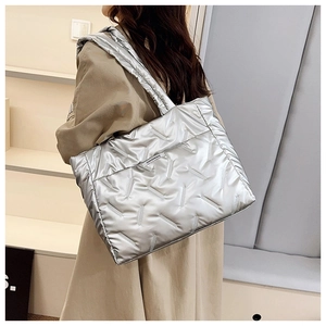 Side view of a silver quilted puffer tote bag worn by a model in a minimalist store