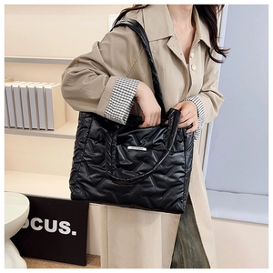 Detail of black quilted puffer tote bag showing geometric stitching and wide shoulder strap