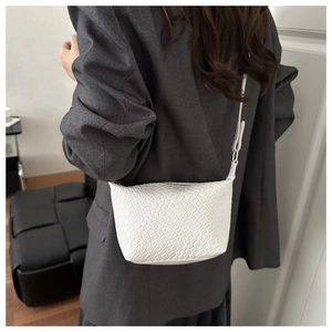 Detail of white woven crossbody bag with slim strap shown on model in modern setting
