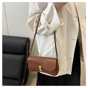 Detail of a brown leather shoulder bag with gold clasp worn with a white textured blazer
