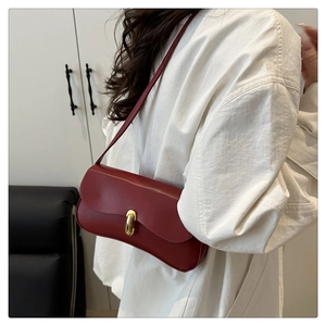 Detail of burgundy leather underarm bag featuring a gold oval lock and slim strap