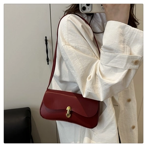 Detail of a dark red leather baguette bag with a stylish golden J-shaped metal buckle lock