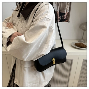 Detail of minimalist black leather underarm bag with gold twist lock shown on model