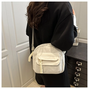 Detail of cream corduroy crossbody bag with woven zipper puller and front pocket