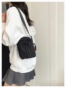 Detail of black nylon drawstring crossbody bag with orange fashion tag and logo