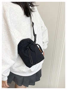 Detail of black nylon crossbody bag with drawstring closure and orange fashion tag