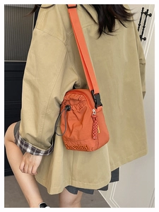 Detail of orange nylon bucket bag featuring drawstring closure and letter embroidery