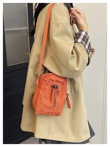 Detail of vibrant orange nylon crossbody bag with drawstring closure and Duoning embroidery