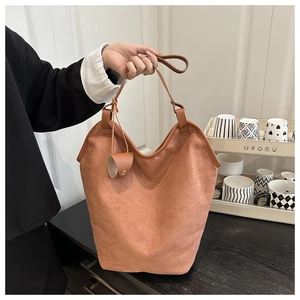 Close-up of brown suede bucket bag with leather trim and long handles in a lifestyle setting