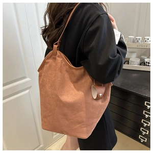 Detail of caramel brown suede tote bag with leather pendant charm in a lifestyle setting