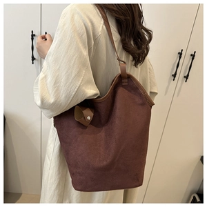 Deep brown faux suede bucket bag shown on shoulder in a minimalist indoor setting