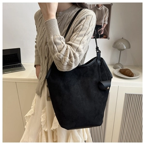 Minimalist black suede bucket tote bag with decorative charm shown in a lifestyle office setting
