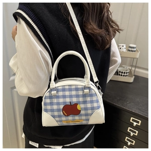 Close-up of blue plaid shell handbag featuring a red apple print and sleek white leather trim