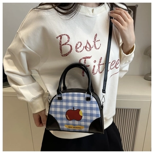 Detail of blue plaid crossbody bag with apple graphic and black leather shoulder strap