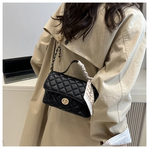 Detail of black quilted handbag with gold chain strap and decorative silk scarf
