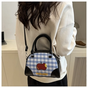 Detail of blue plaid crossbody bag with red apple print worn by model for scale