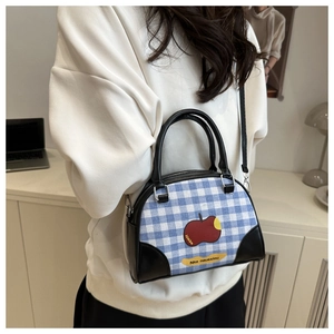Detail of blue plaid canvas crossbody bag with red apple patch and leather handles