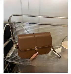 Detail of brown leather baguette bag with golden metal buckle and retro saddle silhouette