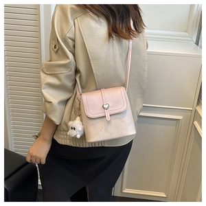 Crossbody bag with silver heart lock and plush ball pendant shown on model