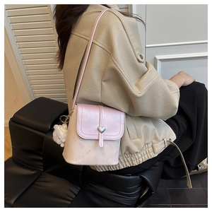 Detail of pink crossbody bucket bag with heart lock and white pompom on model