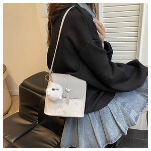 Crossbody bag detail with heart buckle and plush ball charm on a grey patchwork surface