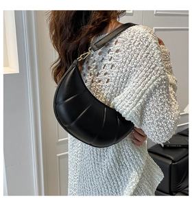 Detail of black pleated croissant shoulder bag with gold hardware buckle and leather texture