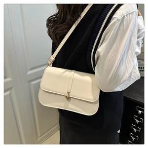 Detail of cream baguette bag with adjustable strap and golden turn-lock closure