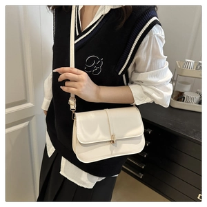 Minimalist beige leather crossbody bag with golden metal buckle on stylish outfit