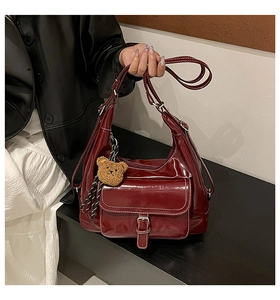 Detail of burgundy hobo bag with contrast stitching and brown plush bear charm accessory