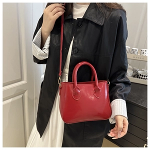 Detail of red patent leather handbag with gold hardware shown on a model for size comparison