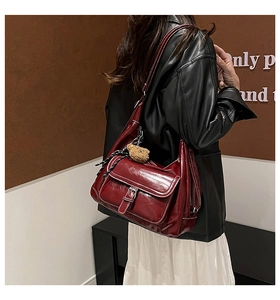 Detail of burgundy glossy leather tote bag with vintage buckle and bear pendant shown on model