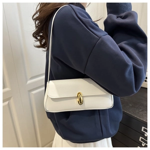 Close-up of a white leather baguette bag with a gold U-shaped metal buckle and lychee texture
