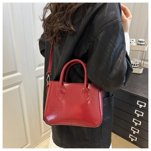 Detail of red patent leather handbag featuring glossy finish and light gold buckles