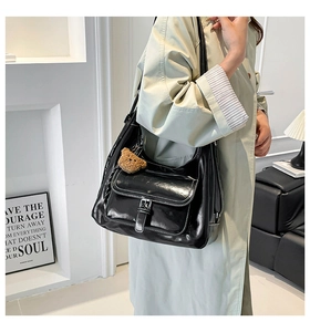 Detail of black glossy PU leather shoulder bag with white stitching and bear charm