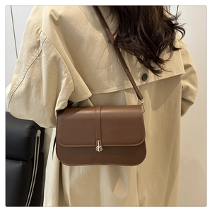 Detail of vintage brown leather bag with golden clasp worn on shoulder by model