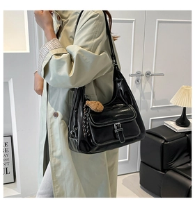 Close-up of black glossy shoulder bag with a cute plush bear charm and buckle pocket