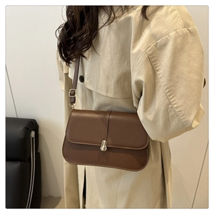 Close-up of a brown vintage baguette bag with gold metal buckle on a beige trench coat