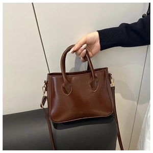 Detail view of glossy dark brown patent leather handbag with dual cylindrical handles