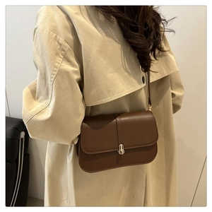 Detail view of a vintage dark brown baguette bag with a gold twist lock on a beige trench coat