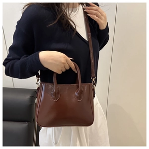 Detail of glossy brown patent leather trapezoid bag with golden hardware and handles