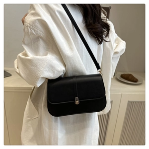 Detail of minimalist black baguette bag with gold metal clasp on a leather shoulder strap