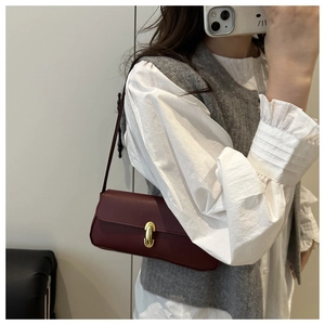 Detail of burgundy leather shoulder bag featuring a gold metal twist lock and pebble texture