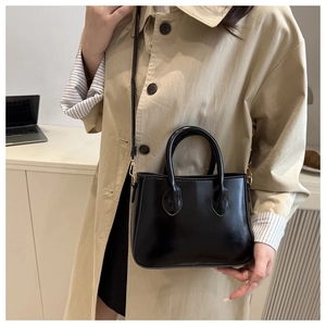 Glossy black patent leather handbag with a sleek handle held by a model in a trench coat