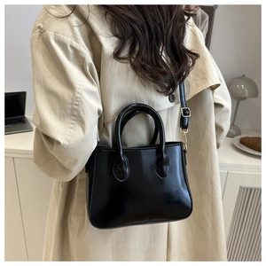 Detail view of a black glossy crossbody bag worn by a model in a modern office setting