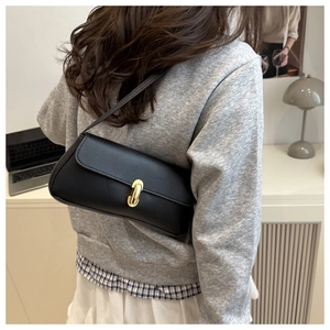 Close-up of black lychee leather underarm bag with gold metal buckle on female model